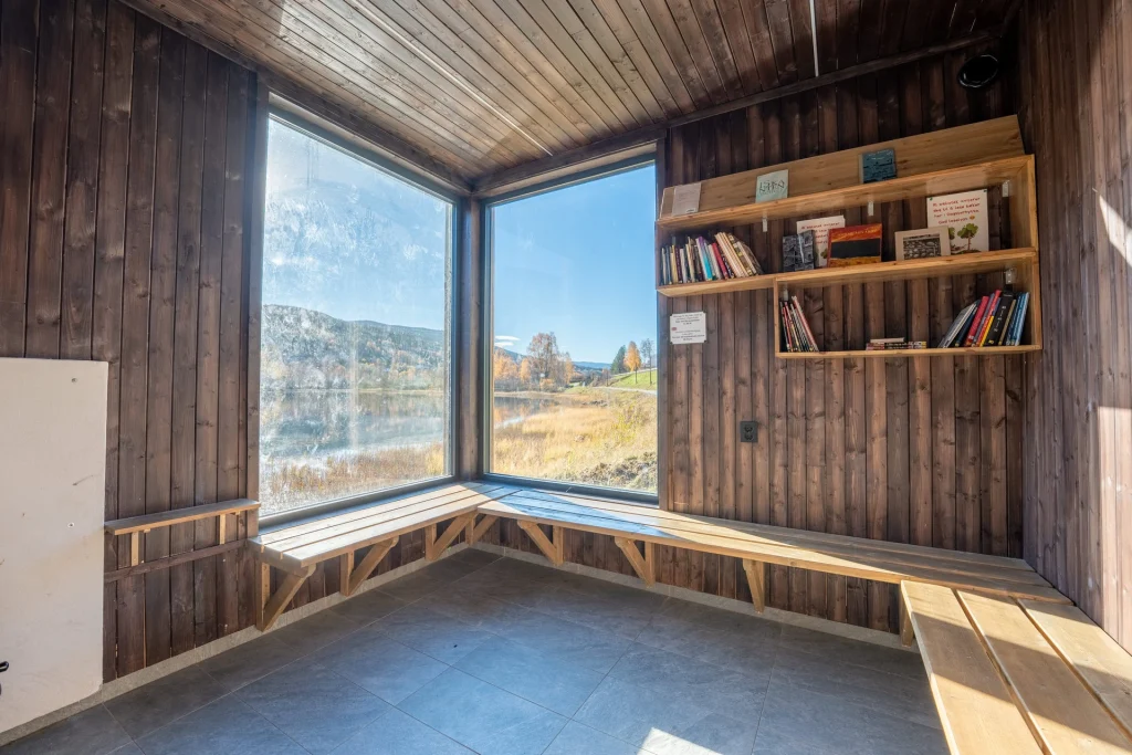Foto tatt inne i dagsturhytta med utsikt ut gjennom to skråstilte vinduer. Det er sol og blå himmel ute.