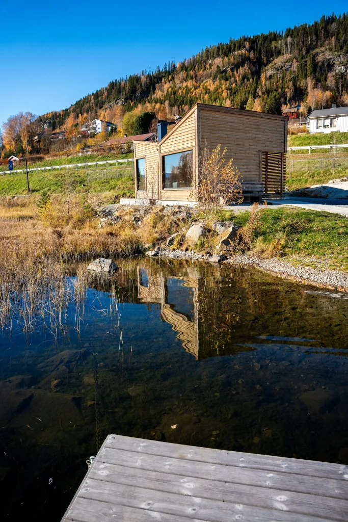 Bilete av badstova tatt frå vatnet. Vatn i front, deretter bygget. turstigen Elvelangs i bakgrunnen.