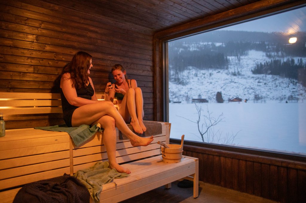 To kvinner som sit ved sidan av kvarandre på benk i badstova.